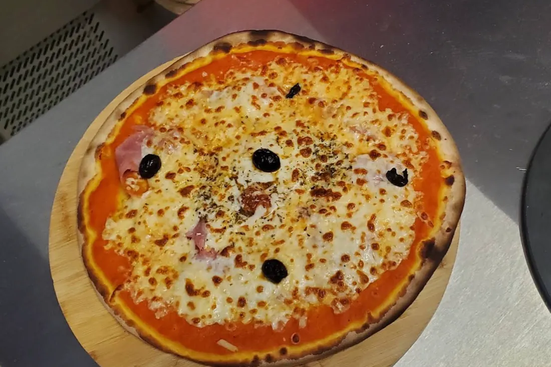 Une pizza au jambon et aux olives sur une planche en bois, chez Pizza Lanka